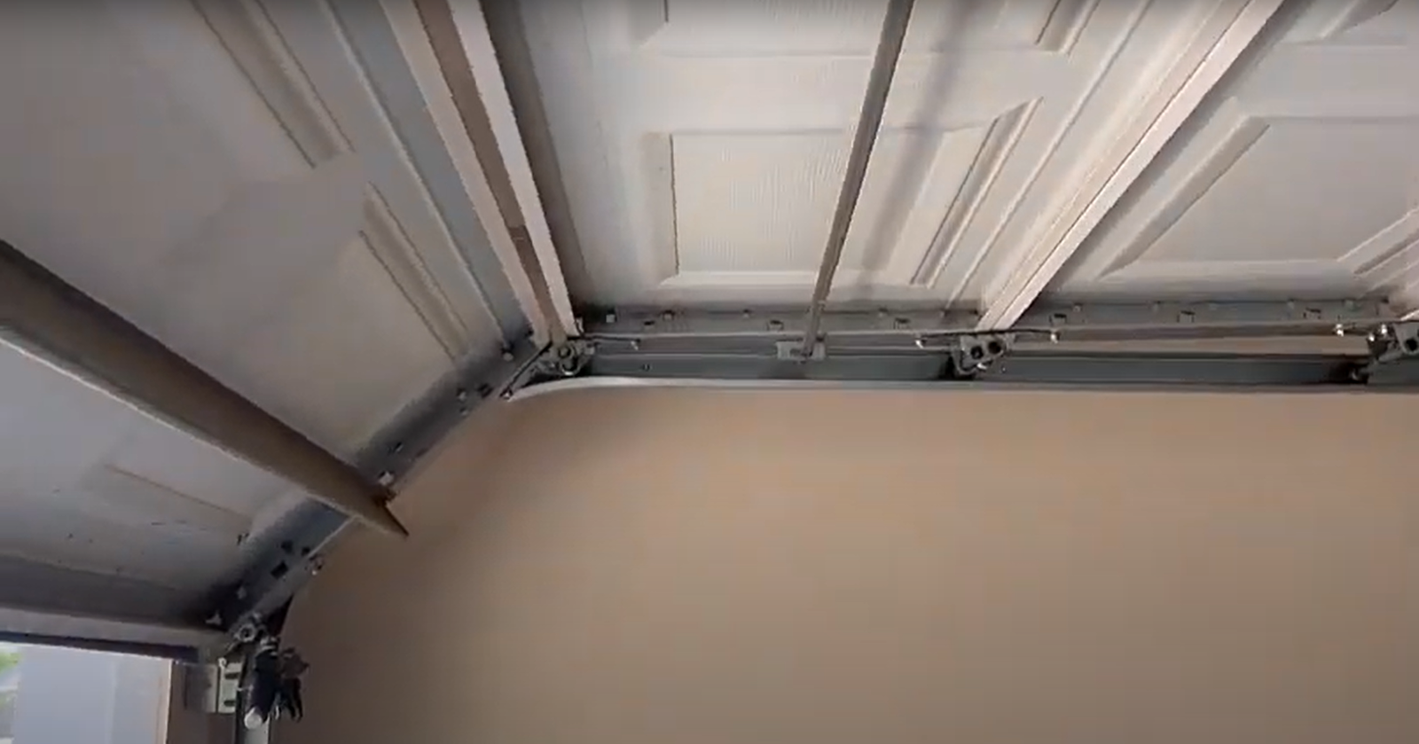 Alt text: A technician performing overhead garage door repair on a residential house.