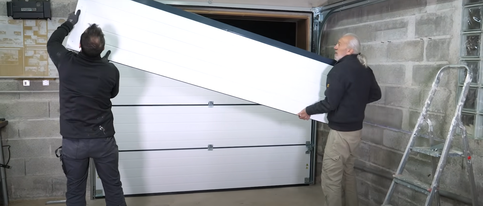 A garage door technician replacing a damaged section of a white garage door.